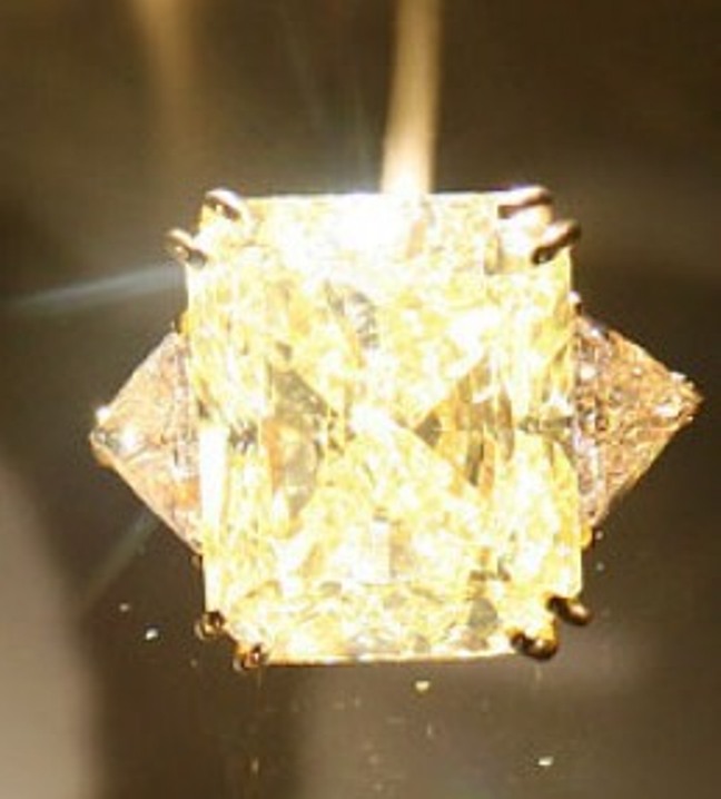 Yellow-gold ring set with a 61.12-carat, starburst-cut fancy yellow diamond flanked by triangular-cut colorless diamonds 